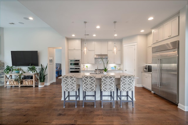 kitchen featuring decorative light fixtures, appliances with stainless steel finishes, a kitchen breakfast bar, an island with sink, and white cabinets