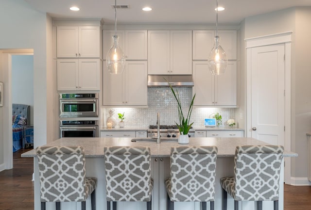 kitchen featuring light stone counters, a kitchen breakfast bar, decorative light fixtures, and an island with sink