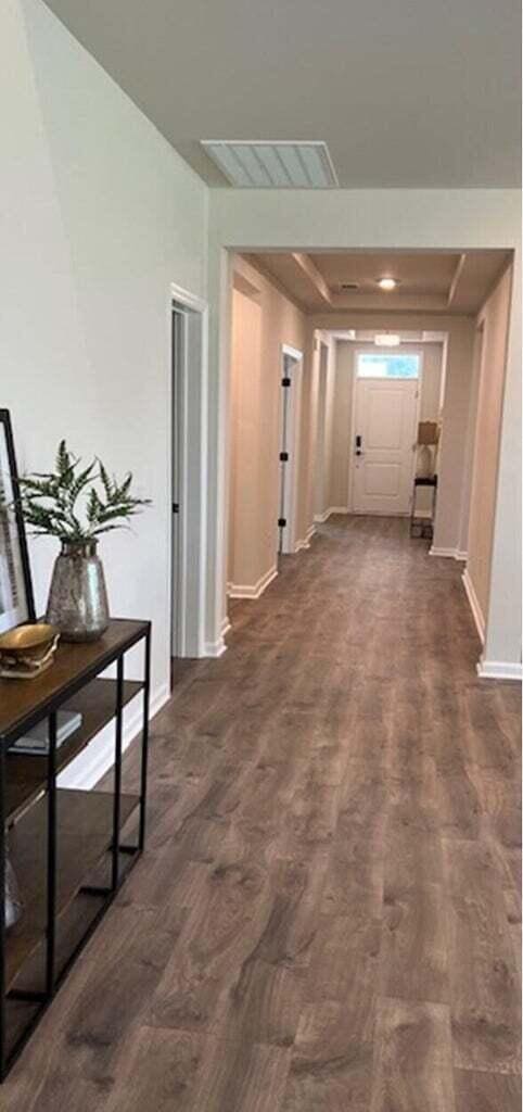 hall with visible vents, dark wood-type flooring, and baseboards