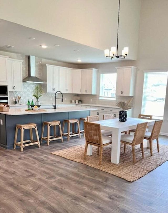 kitchen with a kitchen island with sink, dark wood finished floors, white cabinetry, wall chimney exhaust hood, and decorative backsplash