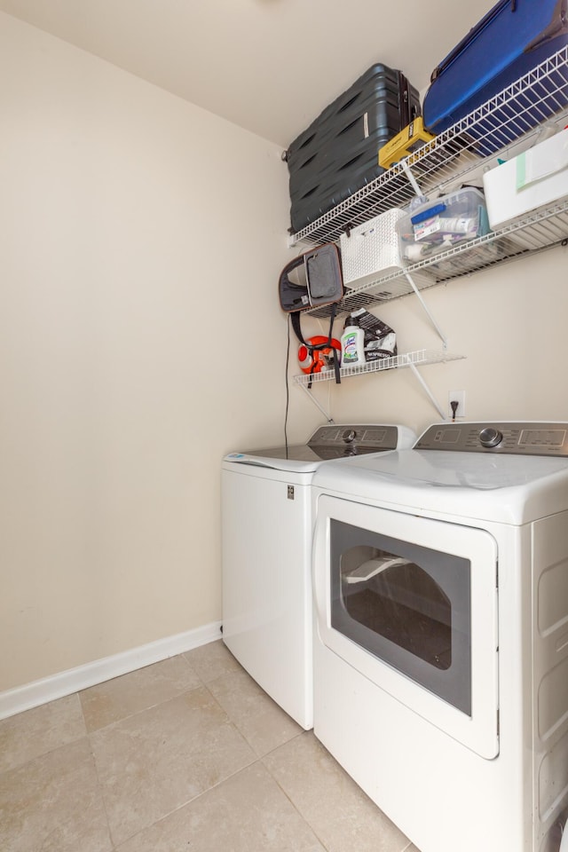 clothes washing area with light tile patterned floors, laundry area, washer and dryer, and baseboards