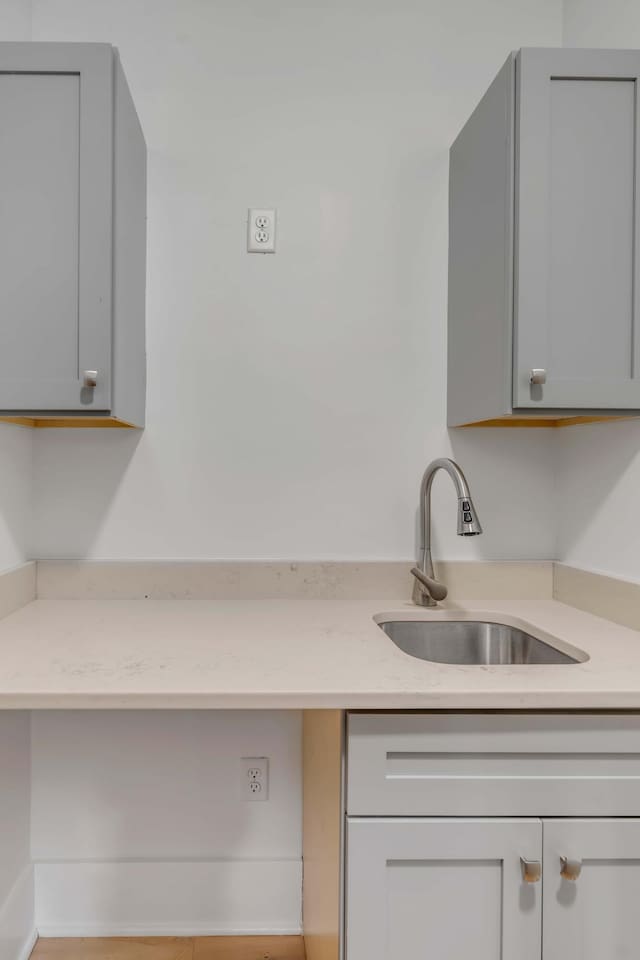 kitchen with a sink, gray cabinetry, and light stone countertops