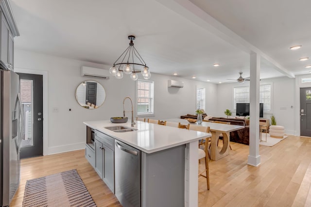 kitchen with appliances with stainless steel finishes, gray cabinets, a wall unit AC, and a sink