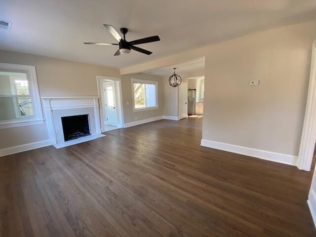 unfurnished living room with ceiling fan with notable chandelier and dark hardwood / wood-style floors