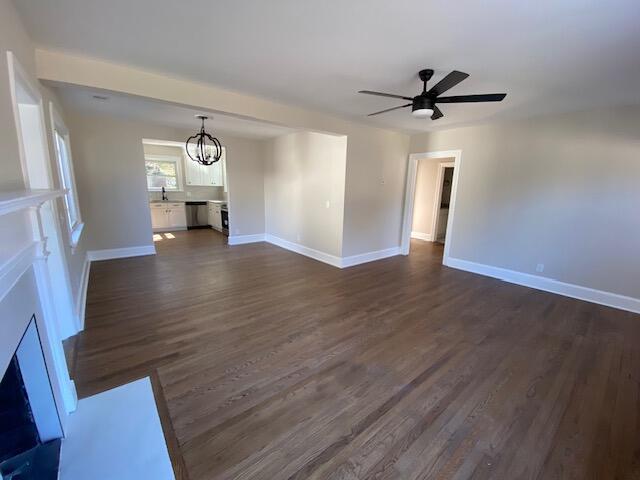 unfurnished living room with dark wood-type flooring, sink, and ceiling fan with notable chandelier