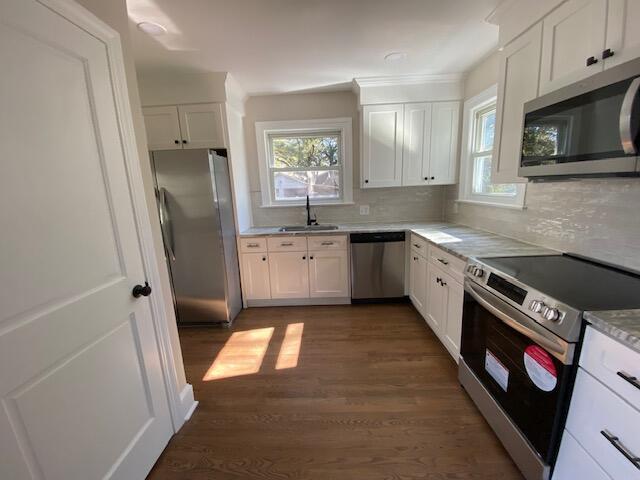 kitchen featuring appliances with stainless steel finishes, sink, white cabinets, dark hardwood / wood-style flooring, and backsplash