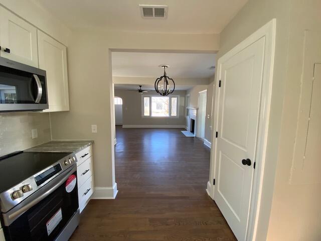 kitchen featuring appliances with stainless steel finishes, white cabinets, hanging light fixtures, light stone counters, and dark wood-type flooring