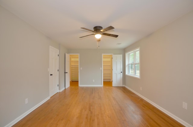 unfurnished bedroom featuring a walk in closet, light hardwood / wood-style flooring, a closet, and ceiling fan