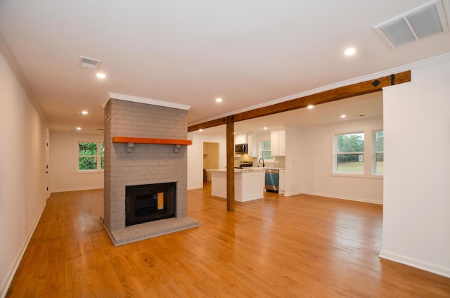 unfurnished living room with crown molding, a brick fireplace, sink, and light hardwood / wood-style flooring