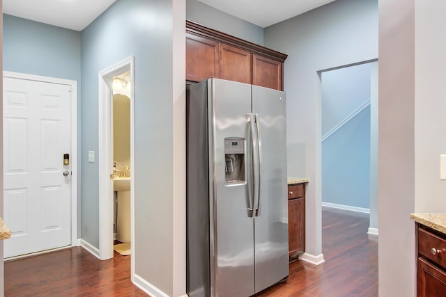 kitchen with dark wood-style floors, baseboards, light stone counters, and stainless steel fridge