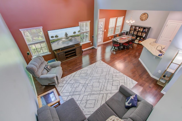 living room with baseboards, vaulted ceiling, an inviting chandelier, and wood finished floors