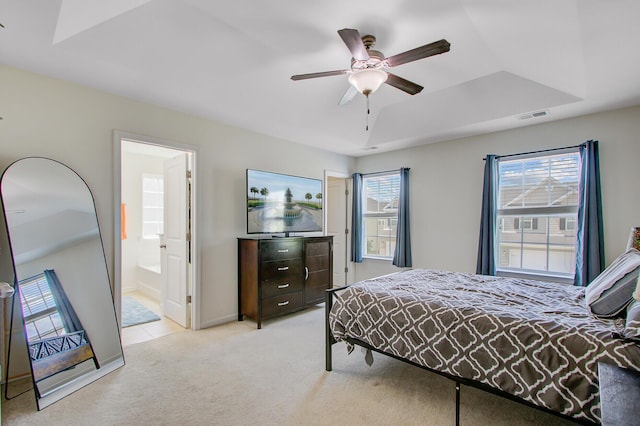 carpeted bedroom featuring visible vents, multiple windows, ensuite bathroom, and a ceiling fan