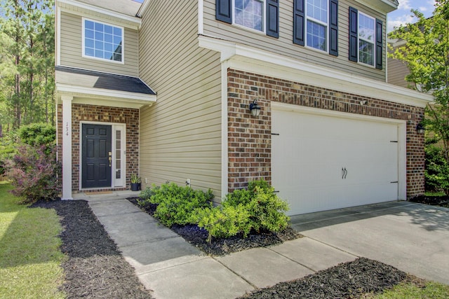 doorway to property with an attached garage, concrete driveway, and brick siding
