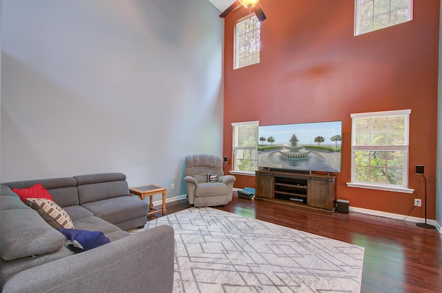 living area featuring a high ceiling, wood finished floors, baseboards, and a healthy amount of sunlight