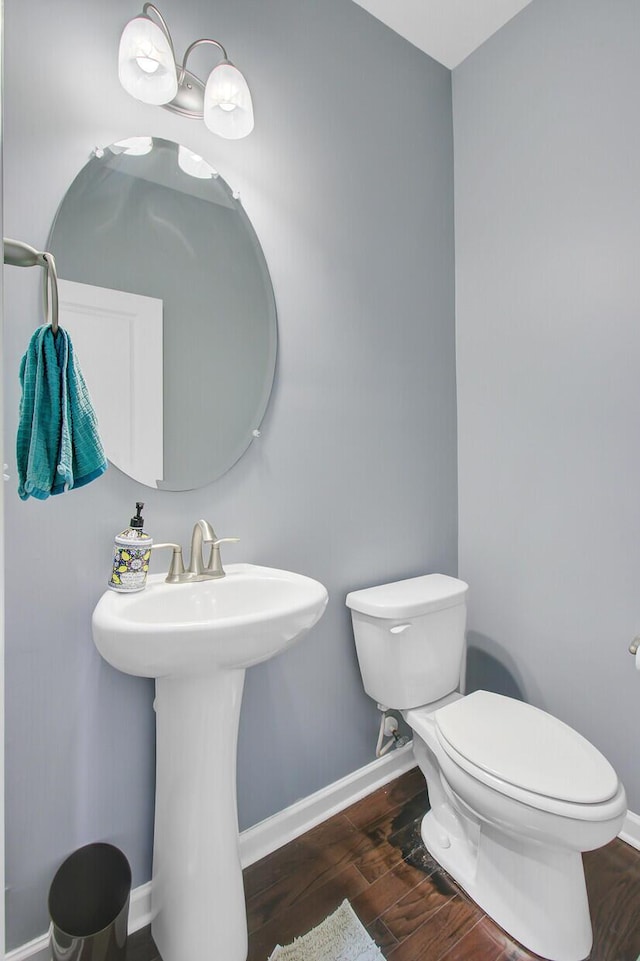half bath featuring baseboards, a sink, toilet, and wood finished floors