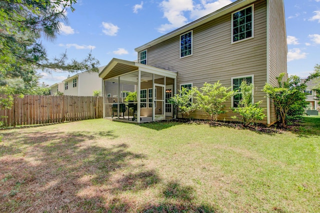 rear view of house featuring a sunroom, fence, and a lawn