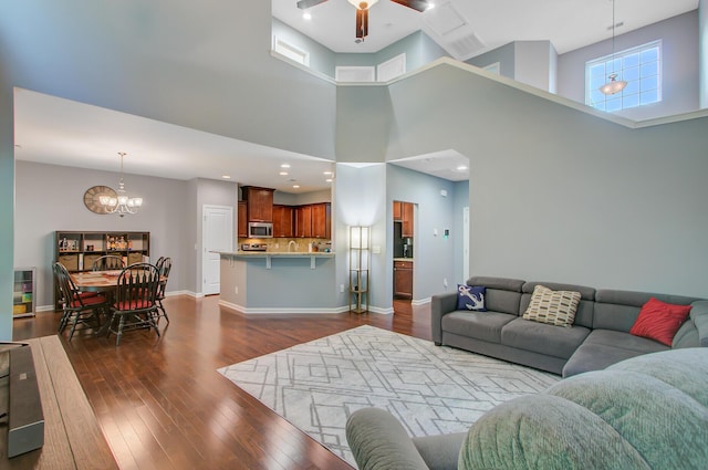 living room with ceiling fan with notable chandelier, recessed lighting, a high ceiling, dark wood-style flooring, and baseboards
