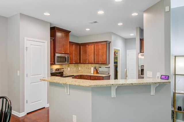 kitchen with tasteful backsplash, a peninsula, dark wood finished floors, stainless steel appliances, and light stone counters