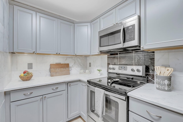 kitchen featuring gray cabinetry, light stone countertops, backsplash, and stainless steel appliances