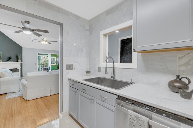 kitchen featuring a sink, stainless steel dishwasher, open floor plan, light wood finished floors, and decorative backsplash