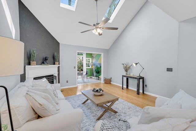 living area featuring high vaulted ceiling, wood finished floors, a skylight, a fireplace, and baseboards