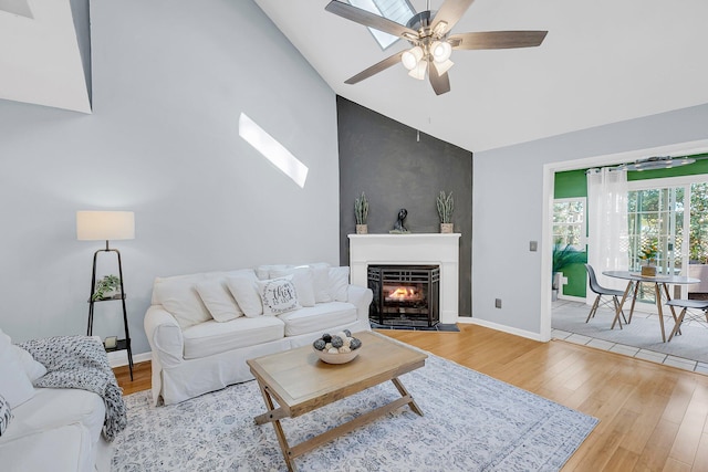 living room featuring ceiling fan, baseboards, a fireplace with flush hearth, wood finished floors, and high vaulted ceiling