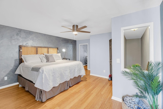 bedroom with ceiling fan, baseboards, an accent wall, and light wood-style floors