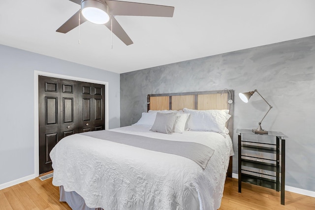 bedroom featuring light wood-style flooring, a closet, baseboards, ceiling fan, and an accent wall