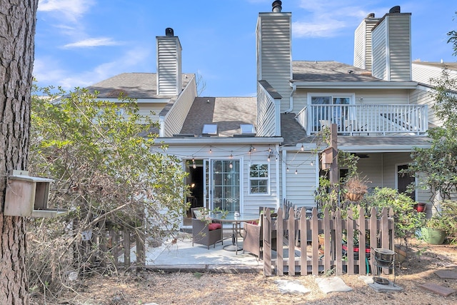 rear view of property with a patio area, a chimney, a balcony, and roof with shingles