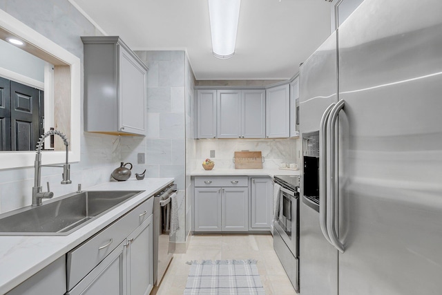 kitchen featuring a sink, backsplash, appliances with stainless steel finishes, and gray cabinets