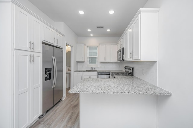 kitchen with stainless steel appliances, tasteful backsplash, white cabinets, light wood-type flooring, and a peninsula