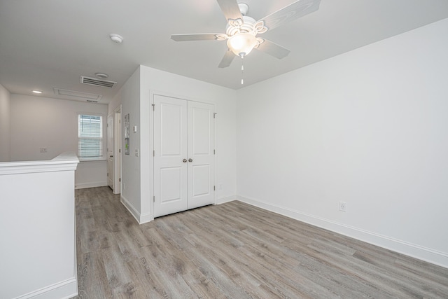 spare room featuring visible vents, a ceiling fan, attic access, light wood-type flooring, and baseboards