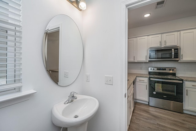 bathroom featuring tasteful backsplash, visible vents, a sink, and wood finished floors