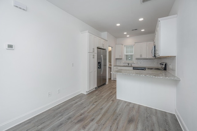 kitchen featuring stainless steel appliances, a peninsula, baseboards, light wood-style floors, and decorative backsplash