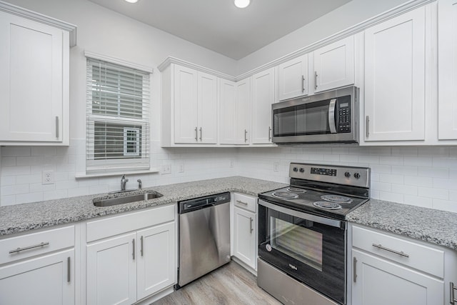 kitchen with tasteful backsplash, white cabinets, stainless steel appliances, light wood-style floors, and a sink