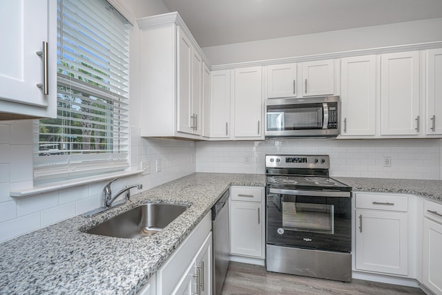 kitchen featuring stainless steel appliances, a sink, white cabinetry, light wood-style floors, and decorative backsplash