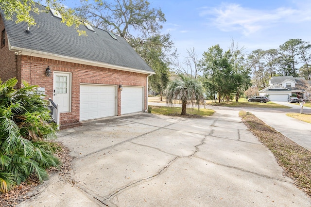 view of side of property featuring a garage, roof with shingles, concrete driveway, and brick siding