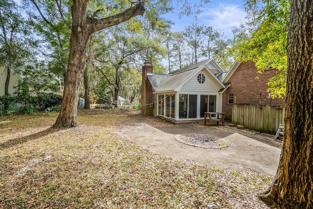 back of house with a sunroom, a chimney, fence, and brick siding