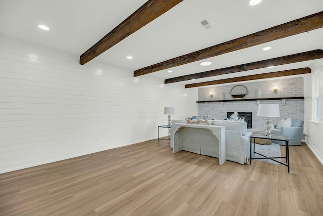 living room with beam ceiling, a brick fireplace, and light wood-type flooring