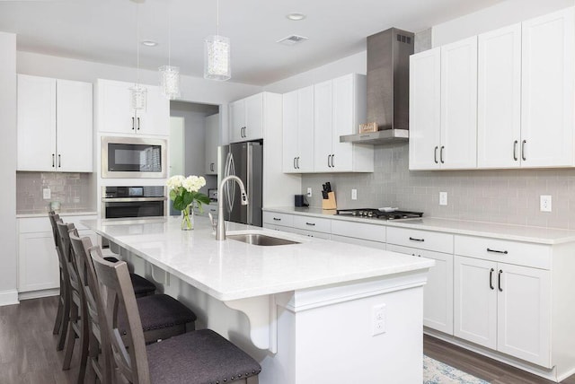 kitchen featuring a kitchen bar, wall chimney range hood, a kitchen island with sink, a sink, and stainless steel appliances