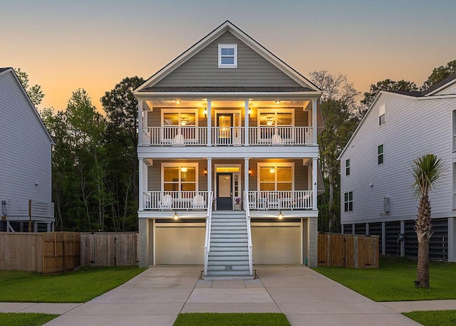 coastal home with a yard, a porch, a garage, concrete driveway, and stairs