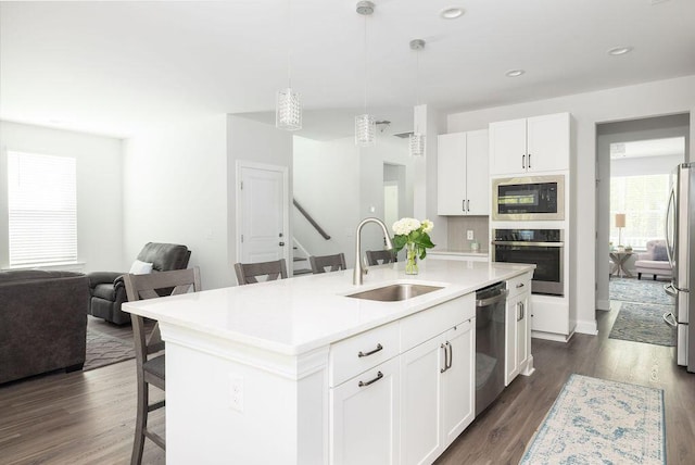 kitchen with an island with sink, a kitchen bar, appliances with stainless steel finishes, a sink, and dark wood-style floors