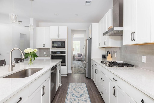 kitchen with wall chimney range hood, white cabinetry, visible vents, appliances with stainless steel finishes, and a sink
