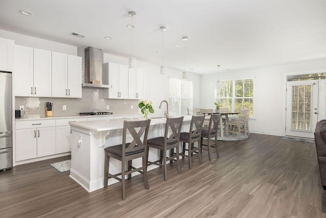 kitchen with light countertops, freestanding refrigerator, backsplash, wall chimney exhaust hood, and gas stovetop