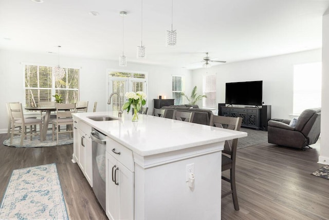 kitchen featuring dishwasher, a sink, ceiling fan, a kitchen bar, and dark wood-style floors