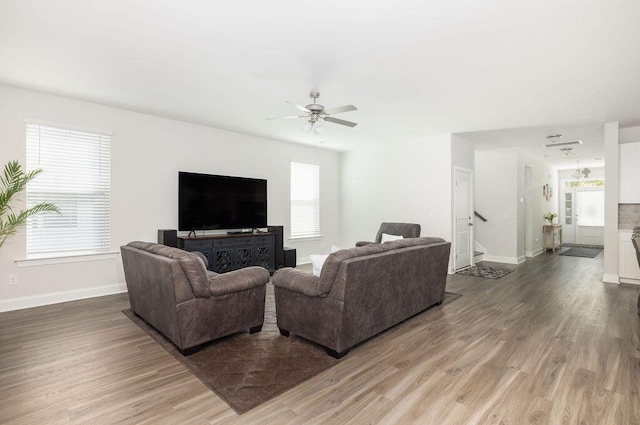 living room with light wood-type flooring, a healthy amount of sunlight, a ceiling fan, and stairs