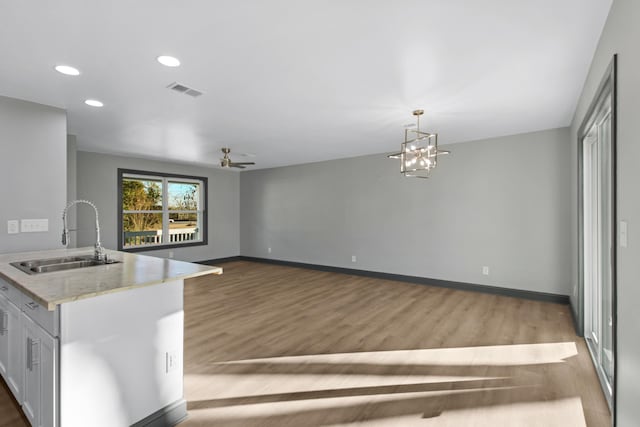 kitchen with ceiling fan with notable chandelier, pendant lighting, white cabinetry, sink, and light hardwood / wood-style flooring