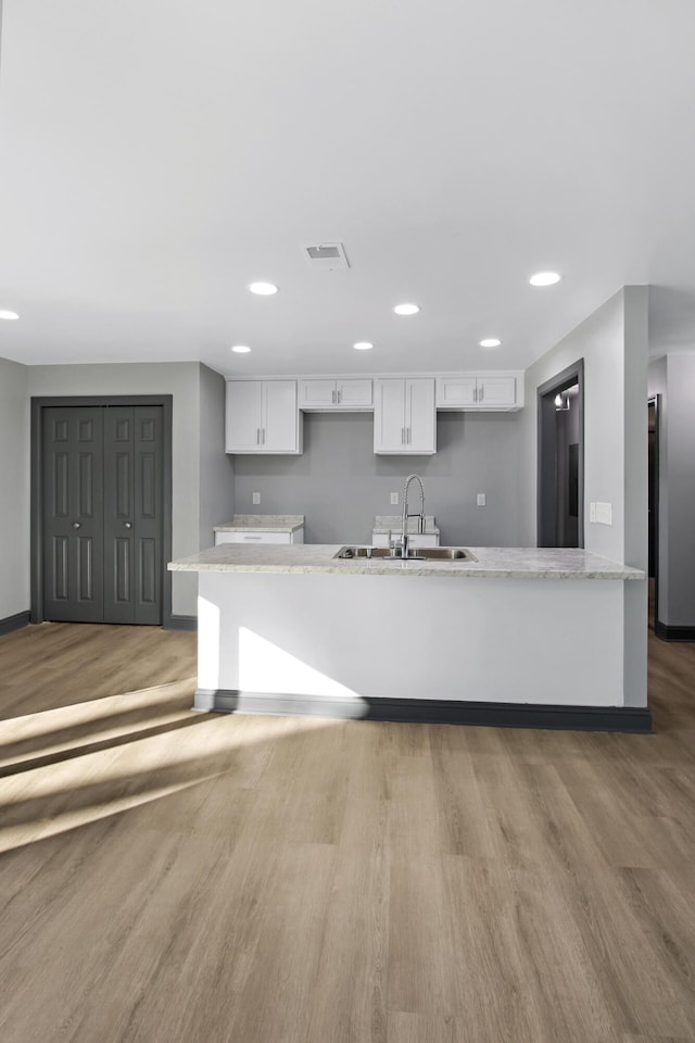 kitchen featuring sink, high end refrigerator, light stone countertops, light hardwood / wood-style floors, and white cabinets