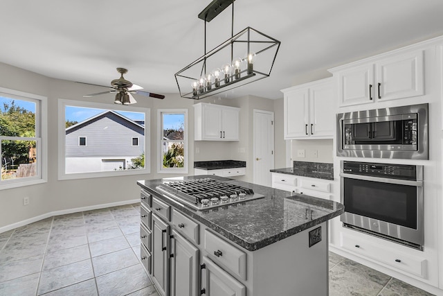 kitchen with baseboards, white cabinets, a ceiling fan, a kitchen island, and appliances with stainless steel finishes