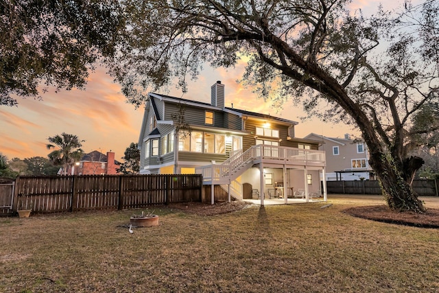 back of property at dusk with a lawn, a fenced backyard, a chimney, stairs, and a wooden deck